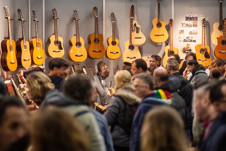 Stand de luthería en una feria nacional con guitarras colgadas, visitantes observando detalles de acabado y un cartel artesanal